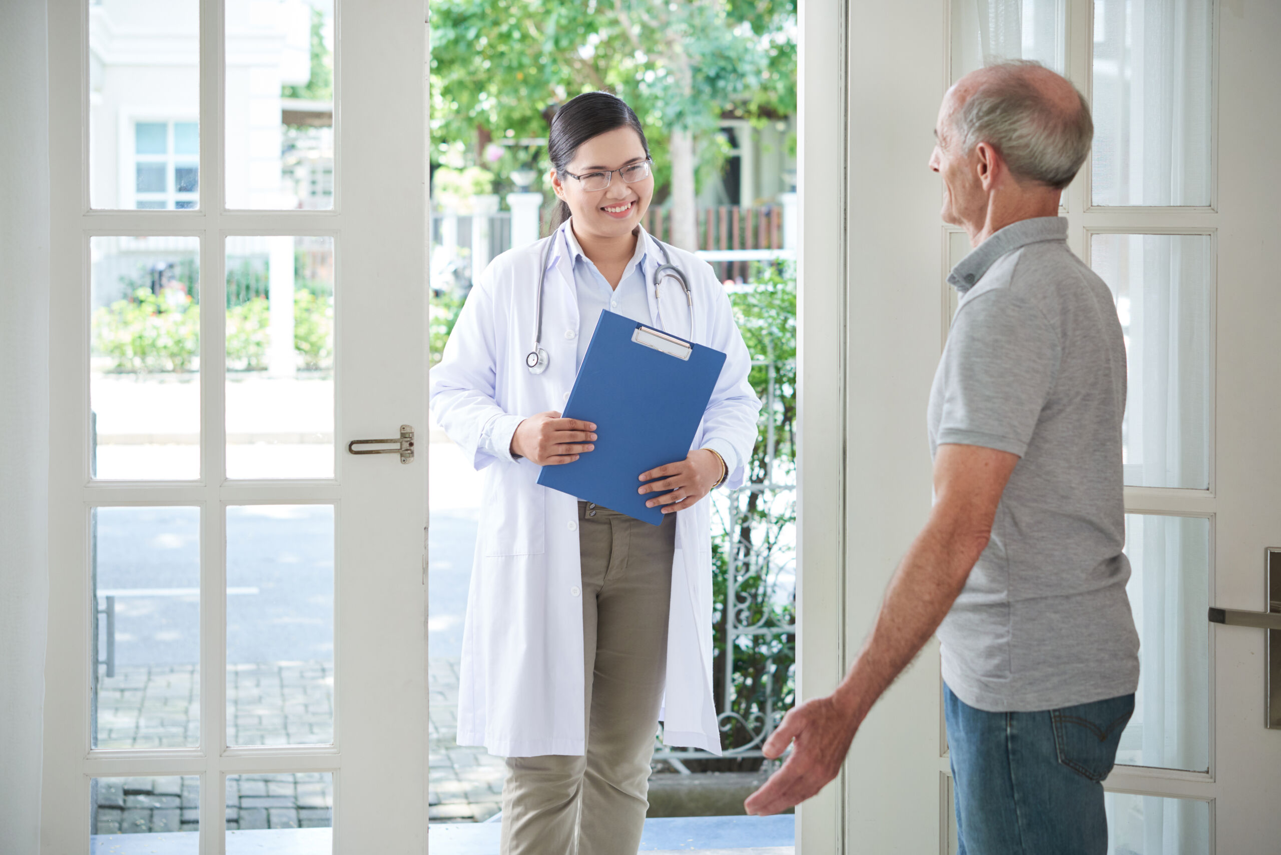 In-Home Therapist Visits & Senior Care Support | Fairhope & Daphne, AL Home health therapist with stethoscope and clipboard arrives at a front door, greeted by an older man for an in-home visit in Baldwin County and Mobile County, Alabama.